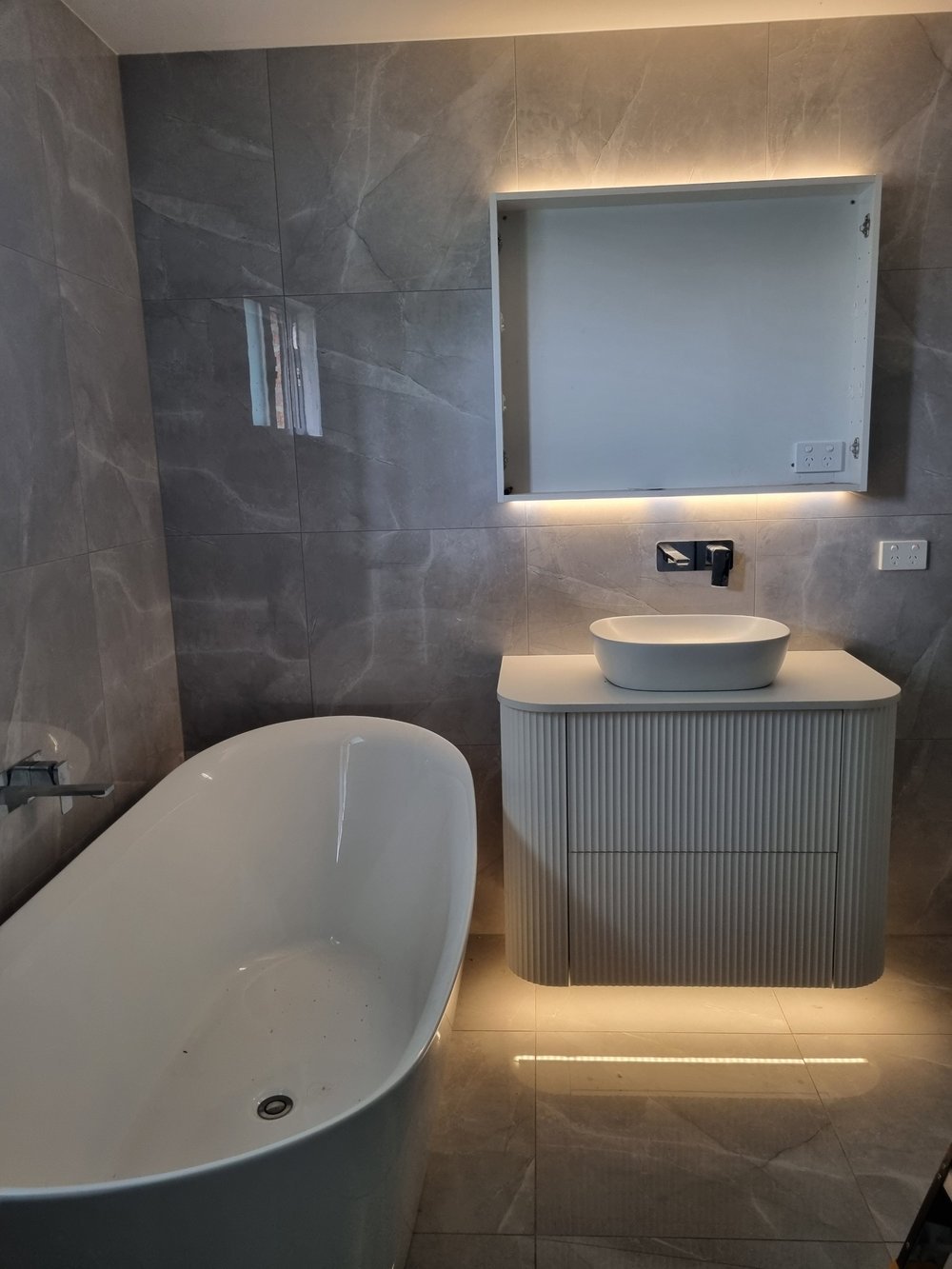 Completed bathroom with illuminated vanity and overhead lighting